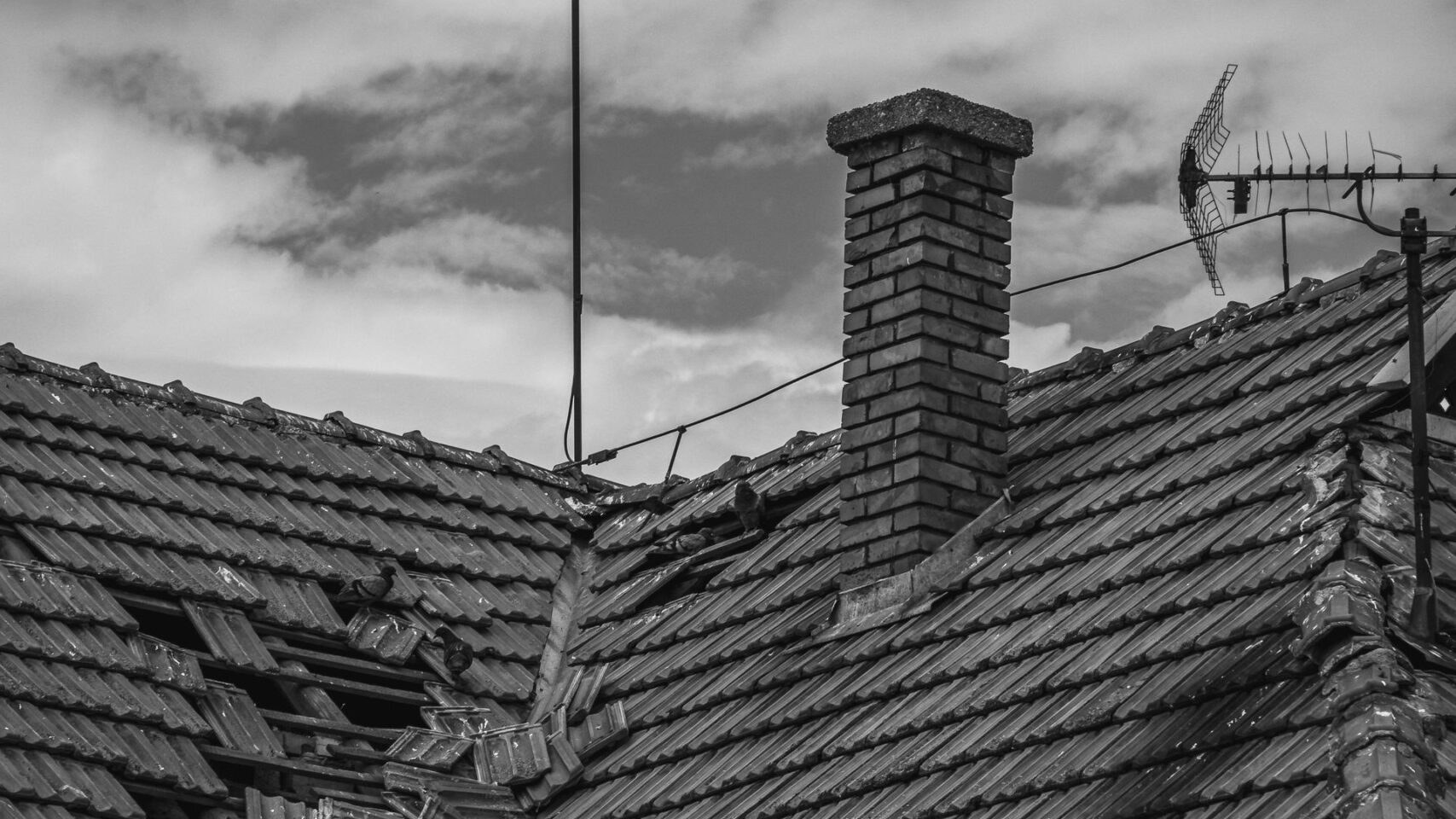 Black and white photo of a storm-damaged roof with tiles dislodged. Black and white photo of a storm-damaged roof with tiles dislodged.
