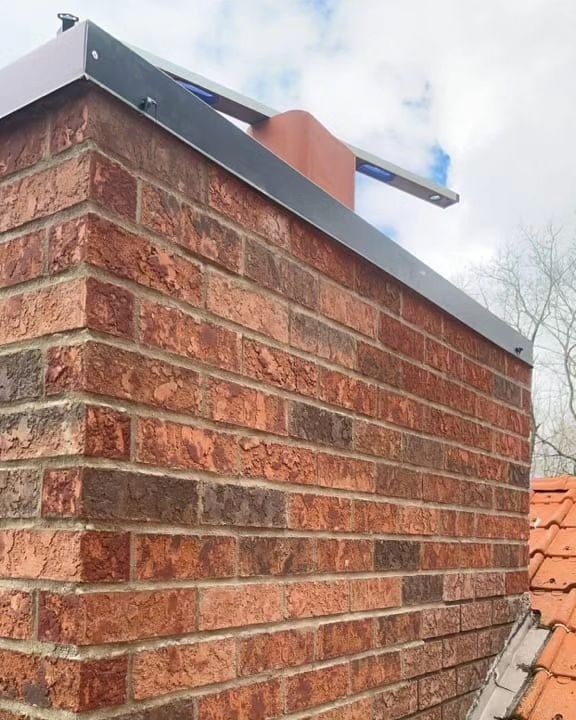 A brick chimney stack fitted with new grey lead flashing and a terracotta pot, seen against a cloudy sky. A brick chimney stack fitted with new grey lead flashing and a terracotta pot, seen against a cloudy sky.