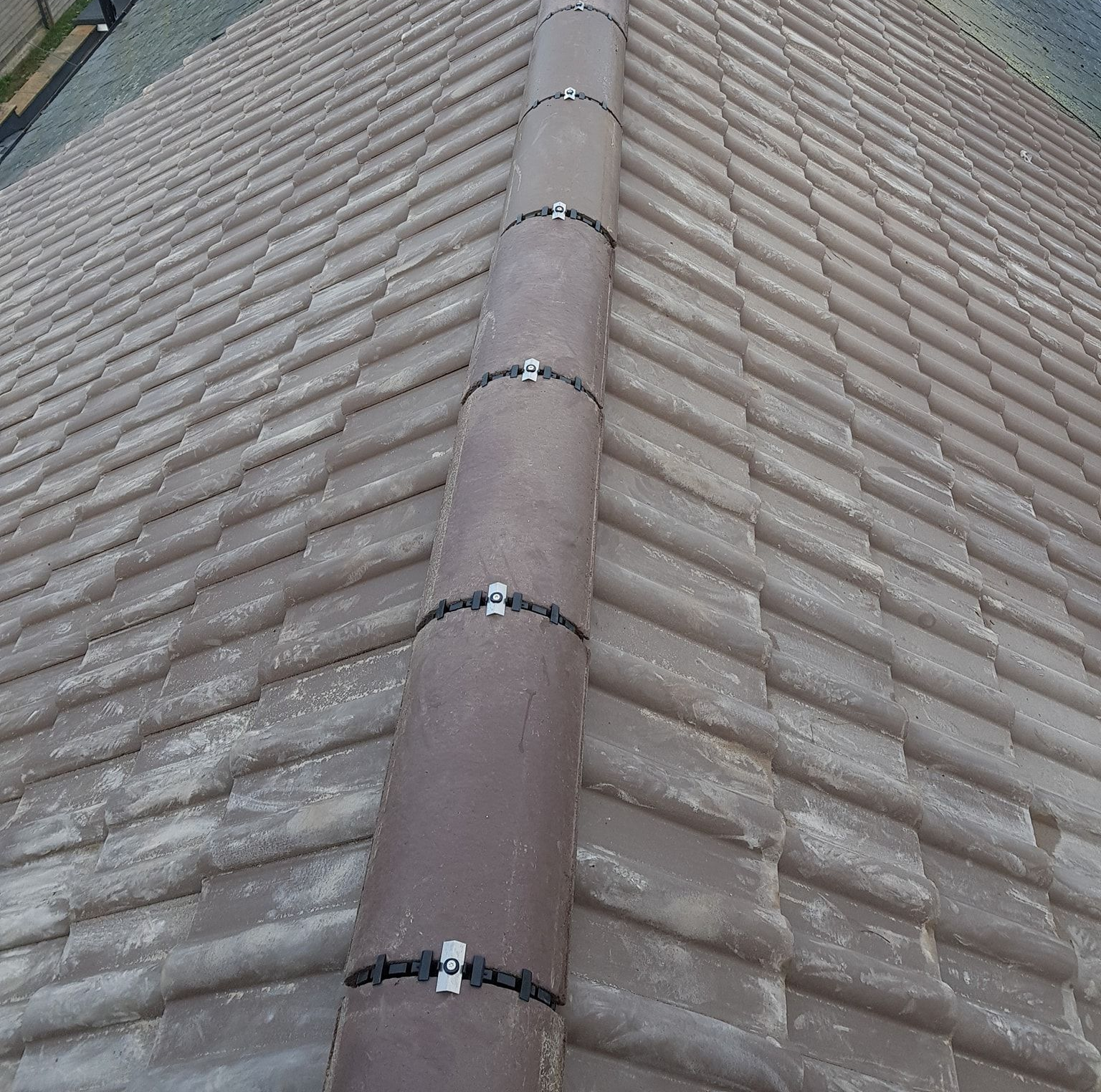 Close-up of ridge tiles secured with stainless steel dry ridge clip fixings instead of mortar. Close-up of ridge tiles secured with stainless steel dry ridge clip fixings instead of mortar.