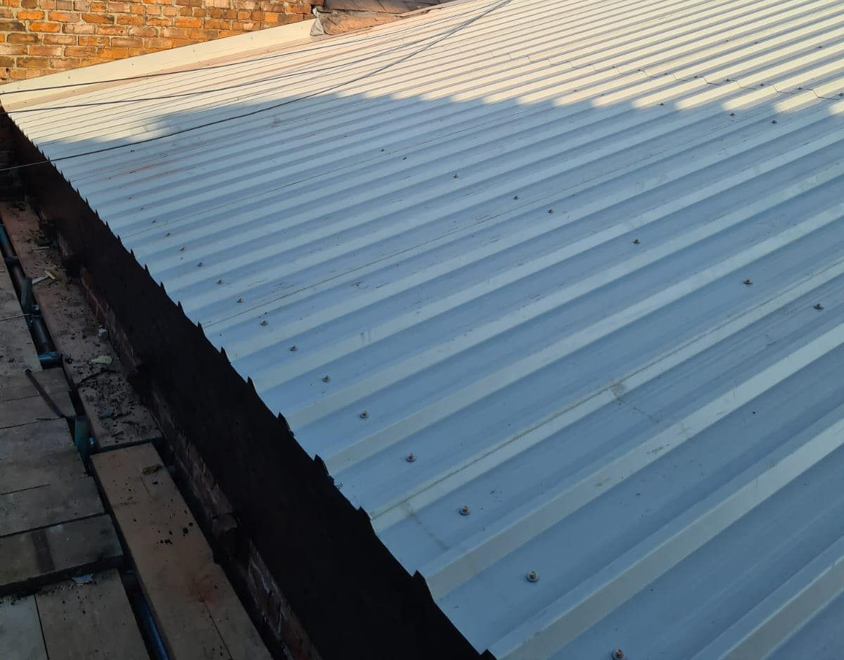 Close-up of newly installed corrugated white metal roof sheeting fixed with screws against a brick chimney stack.