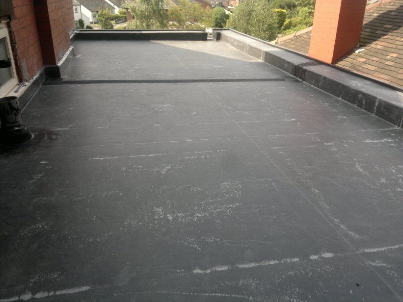A dark grey flat rubber roof on an extension, flanked by brick chimneys and pitched tile roofs.