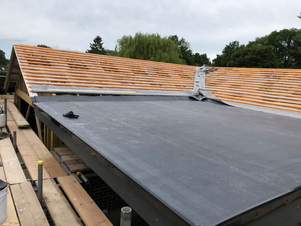A grey EPDM rubber roof membrane fitted over a flat roof section beneath an adjoining pitched roof with exposed timber rafters.