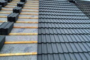 A roof under construction showing grey concrete interlocking tiles laid over timber battens and felt underlay on one side, with exposed battens on the other.