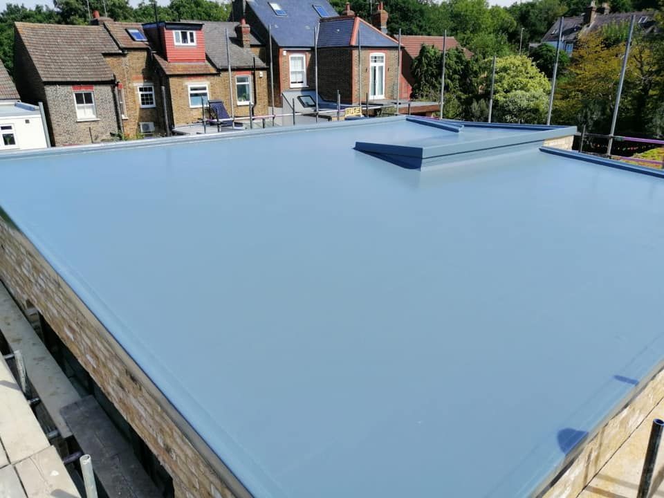 A finished pale grey GRP fibreglass flat roof on a garage with a raised skylight upstand, overlooking terraced houses and trees. A finished pale grey GRP fibreglass flat roof on a garage with a raised skylight upstand, overlooking terraced houses and trees.