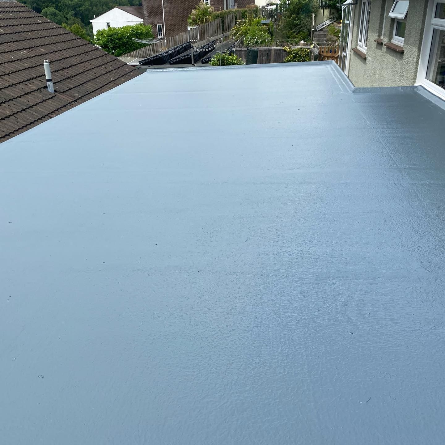 A grey GRP fibreglass flat roof with a chimney stack upstand, alongside a garden fence.