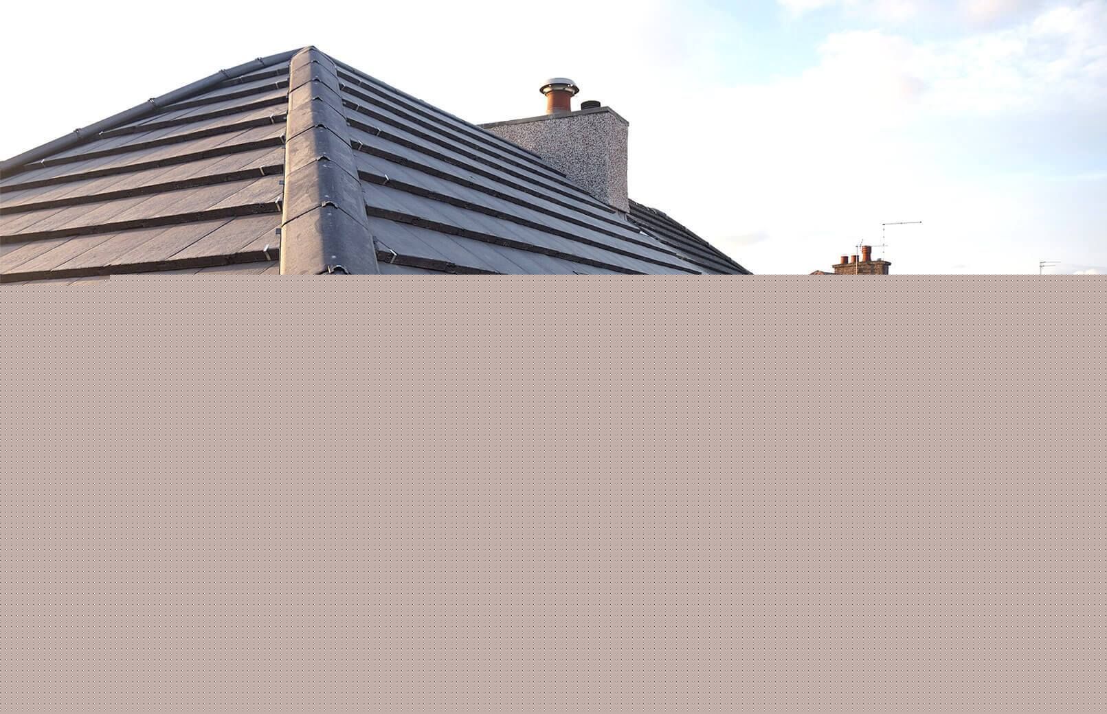A grey tiled hip roof with a brick chimney stack fitted with a vent cap, seen against a cloudy sky. A grey tiled hip roof with a brick chimney stack fitted with a vent cap, seen against a cloudy sky.