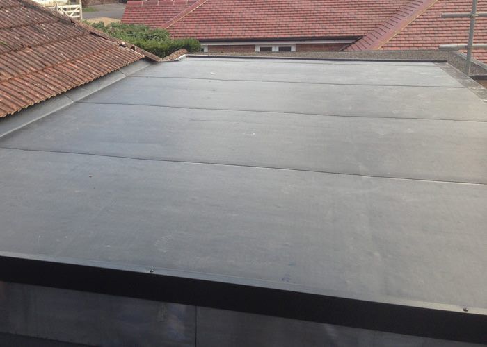 A flat grey EPDM rubber roof adjoining a red clay tiled pitched roof on a terraced house. A flat grey EPDM rubber roof adjoining a red clay tiled pitched roof on a terraced house.