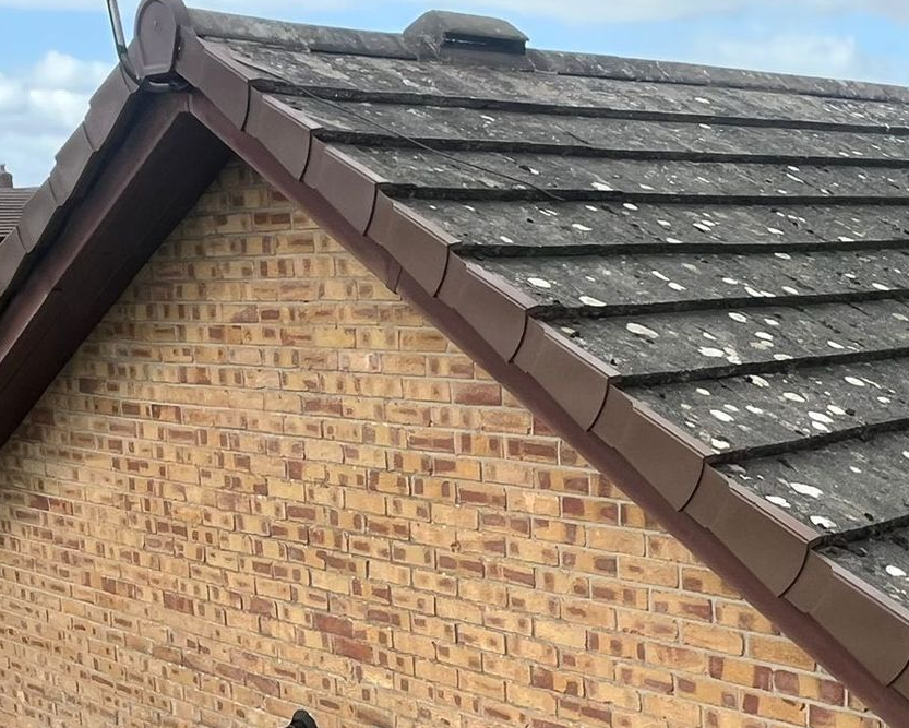 A grey slate tiled roof edge fitted with a brown dry verge system against a brick gable wall.