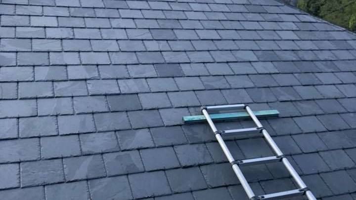 A grey slate roof with a ladder propped up beside a brick chimney stack. A grey slate roof with a ladder propped up beside a brick chimney stack.