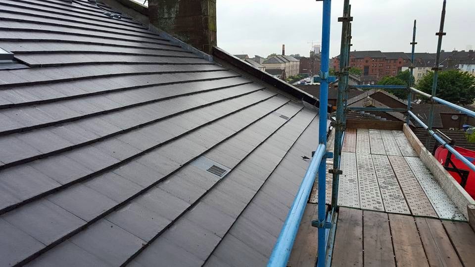 A grey tiled pitched roof under repair with blue scaffolding. A grey tiled pitched roof under repair with blue scaffolding.