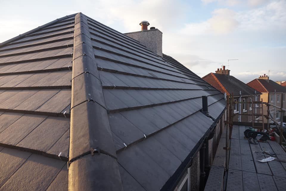 A grey tiled roof with a chimney and scaffolding during fitting work. A grey tiled roof with a chimney and scaffolding during fitting work.