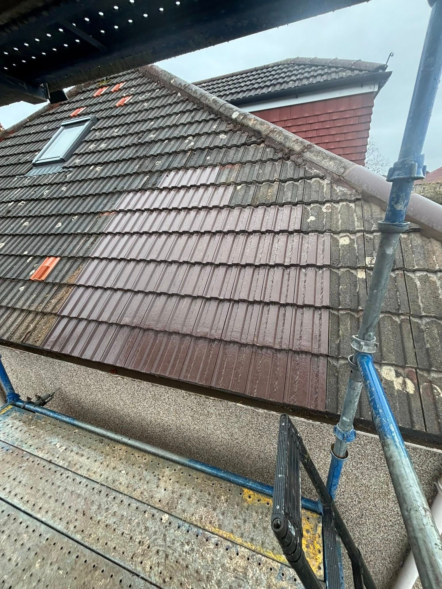 A pitched roof with rows of new reddish-brown tiles replacing older weathered grey tiles, viewed from scaffolding with a skylight visible. A pitched roof with rows of new reddish-brown tiles replacing older weathered grey tiles, viewed from scaffolding with a skylight visible.