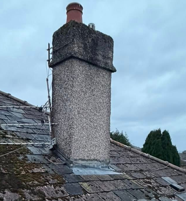A tall pebbledash-rendered chimney stack with a red clay pot rising from a weathered grey slate roof against a cloudy sky. A tall pebbledash-rendered chimney stack with a red clay pot rising from a weathered grey slate roof against a cloudy sky.