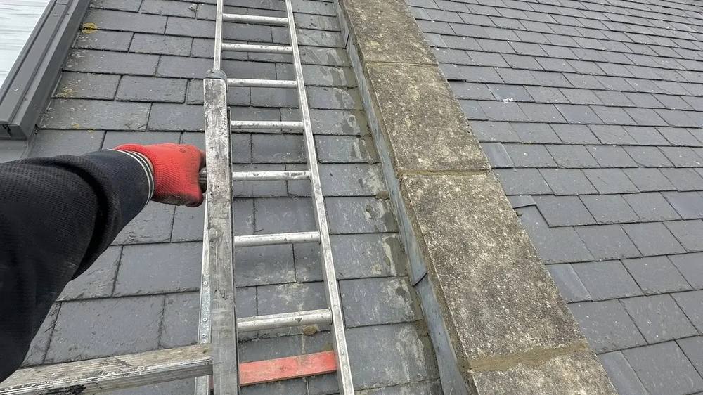A roofer on a ladder working on a chimney stack on a pitched roof. A roofer on a ladder working on a chimney stack on a pitched roof.