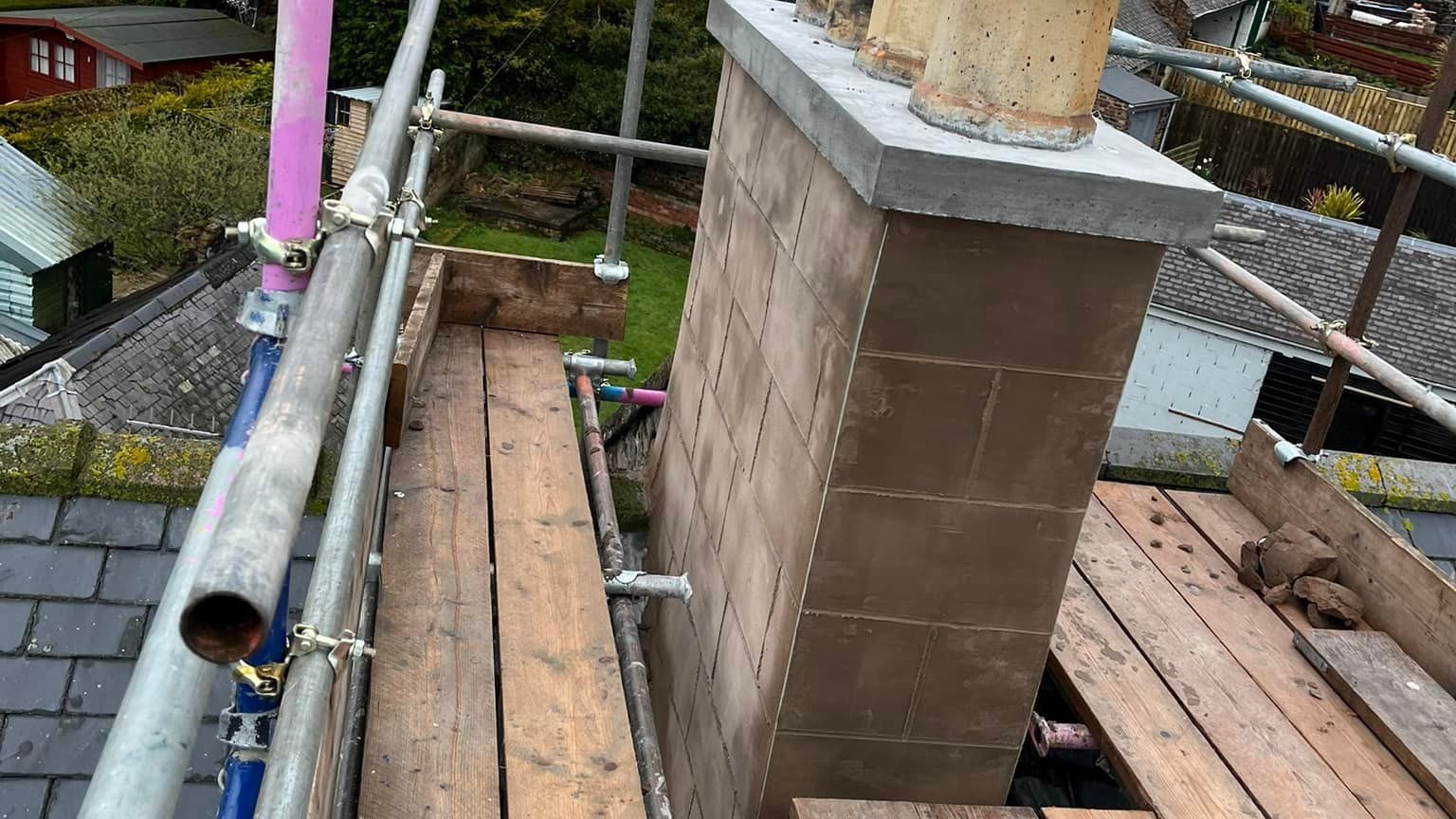 Roofers working from rooftop scaffold boards beside a rebuilt brick chimney stack with three terracotta chimney pots, overlooking a row of nearby houses. Roofers working from rooftop scaffold boards beside a rebuilt brick chimney stack with three terracotta chimney pots, overlooking a row of nearby houses.
