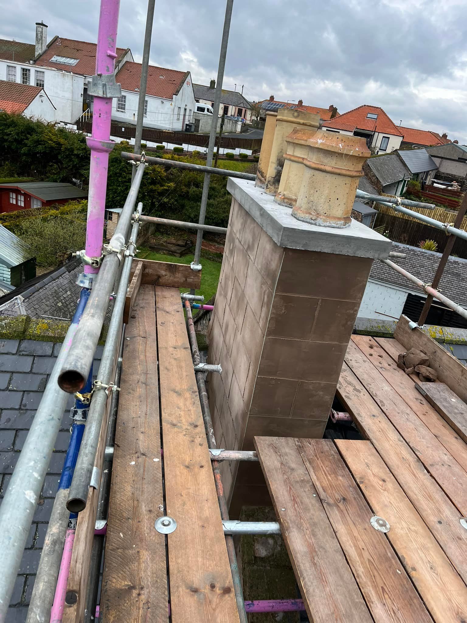 Roofers on scaffolding rebuilding a brick chimney stack during a structural repair Roofers on scaffolding rebuilding a brick chimney stack during a structural repair