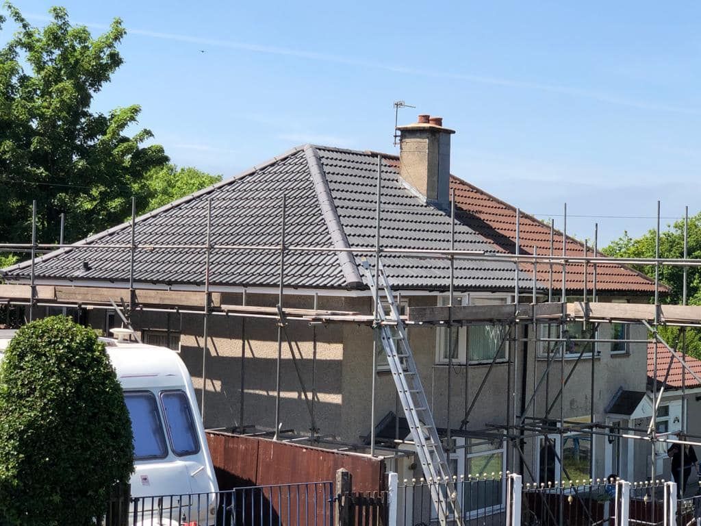 A house with a grey tiled roof and chimney stack surrounded by full scaffolding. A house with a grey tiled roof and chimney stack surrounded by full scaffolding.