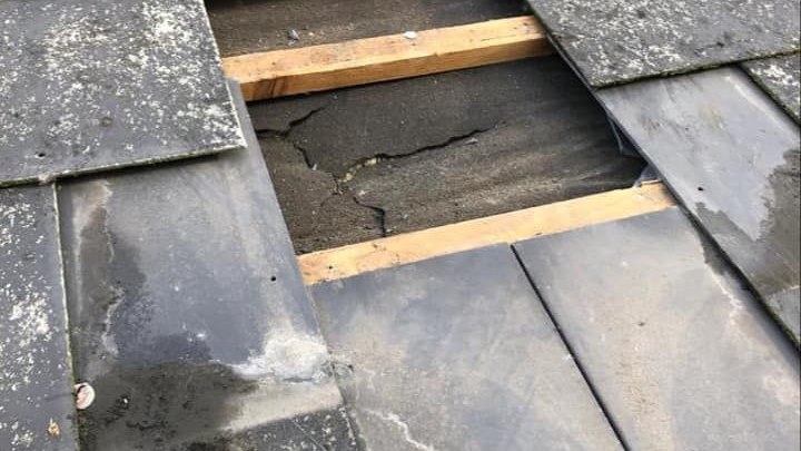 A slate roof with a hole exposing the wooden batten beneath after storm damage. A slate roof with a hole exposing the wooden batten beneath after storm damage.