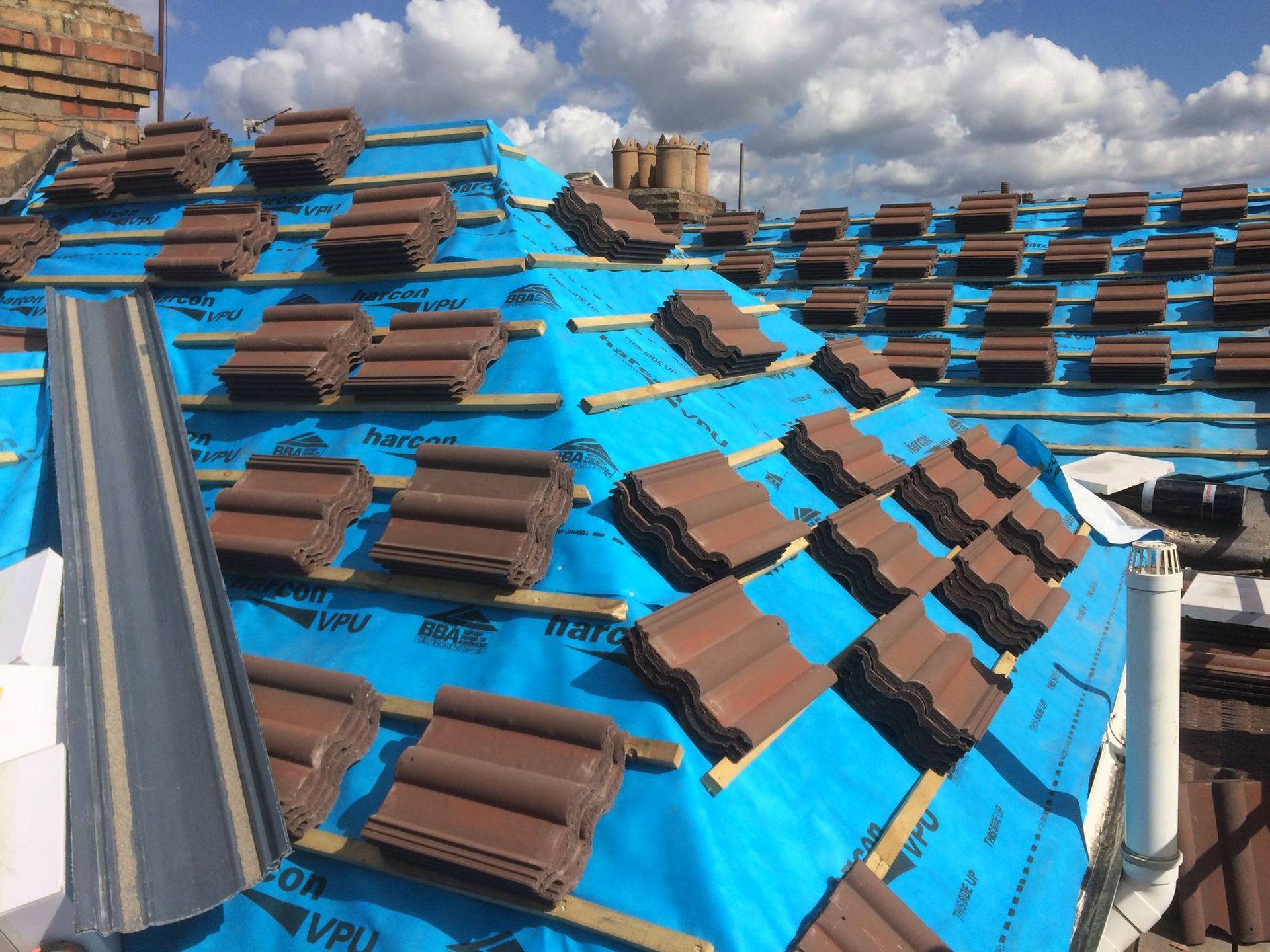 Stacks of new brown roof tiles laid out on timber battens ready for fitting. Stacks of new brown roof tiles laid out on timber battens ready for fitting.