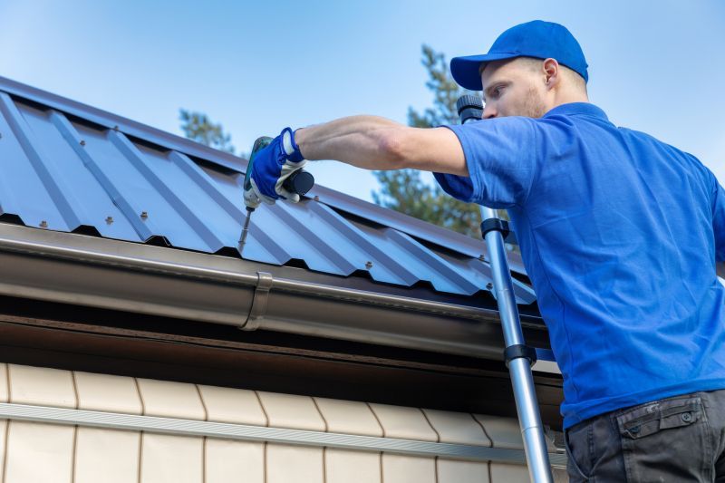 A roofer working on a ladder, drilling and fixing a metal roof sheet in place. A roofer working on a ladder, drilling and fixing a metal roof sheet in place.