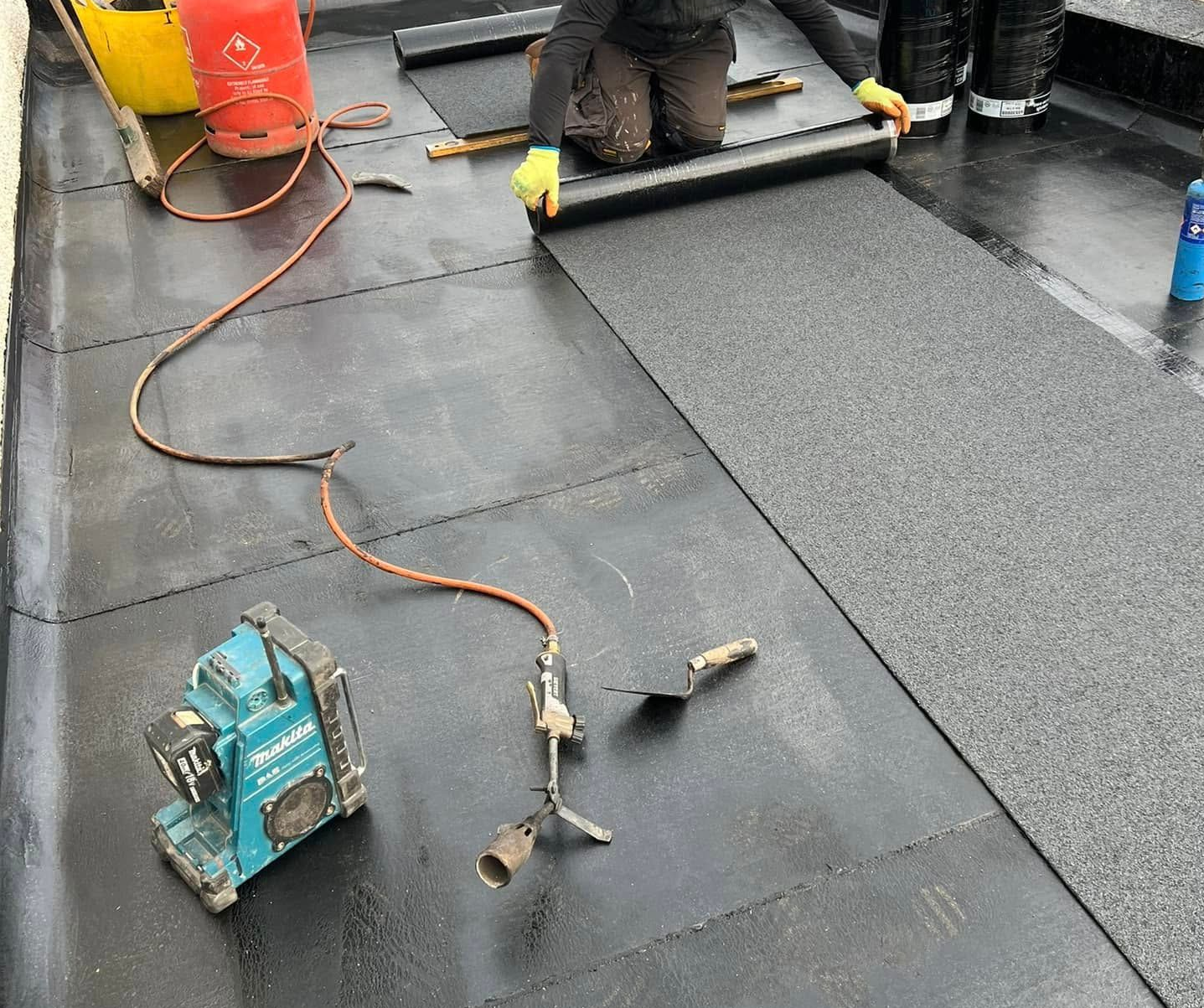 A roofer torching a rubber roof membrane into place during a flat roof installation. A roofer torching a rubber roof membrane into place during a flat roof installation.