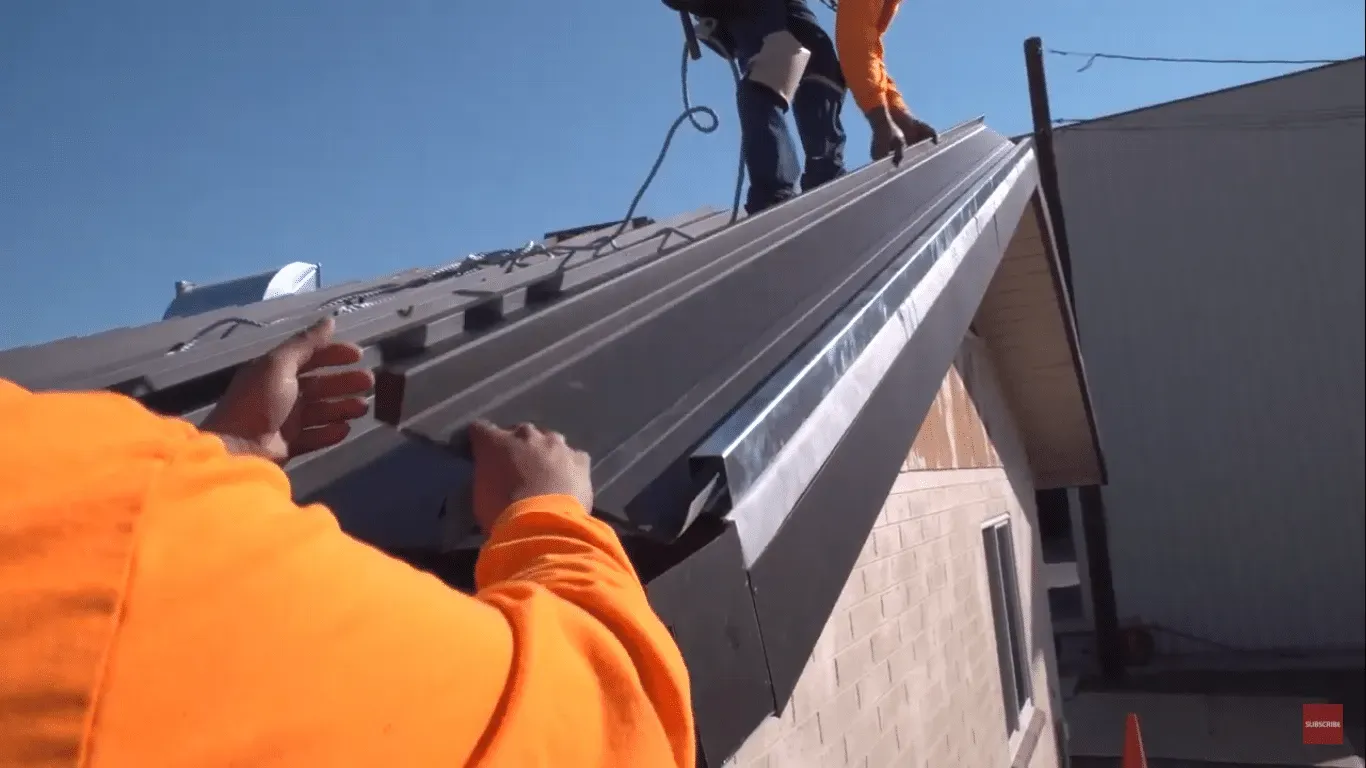 Workers fitting a grey metal standing seam roof on a commercial building.